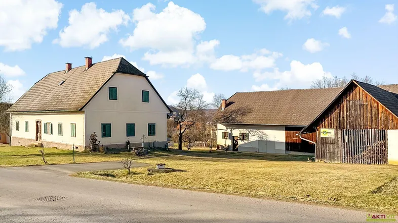 Ländliches Anwesen mit mehreren Gebäuden und weitläufigem Grundstück unter blauem Himmel.