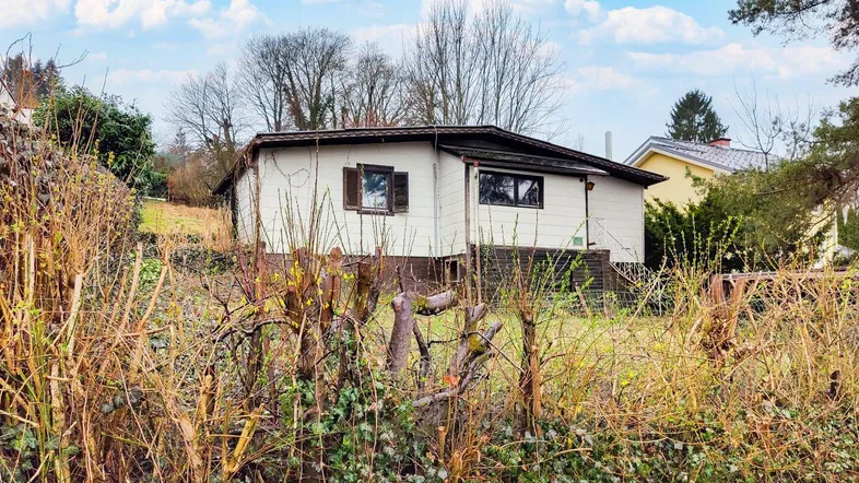 Älteres Einfamilienhaus mit weißer Fassade und dunklem Dach, umgeben von winterlicher Vegetation.