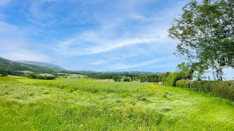 Weitläufige grüne Wiese mit Blick auf die umliegende Landschaft und ferne Hügel unter blauem Himmel.