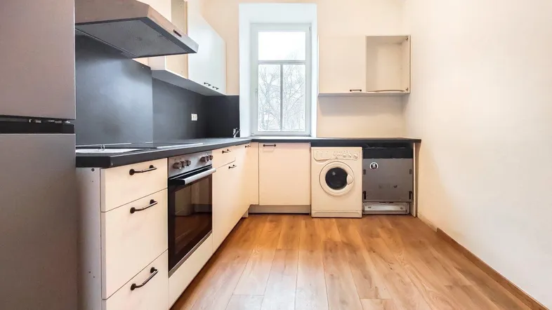 Helle Küche mit Einbaugeräten, Laminatboden und Fenster für natürliches Licht.