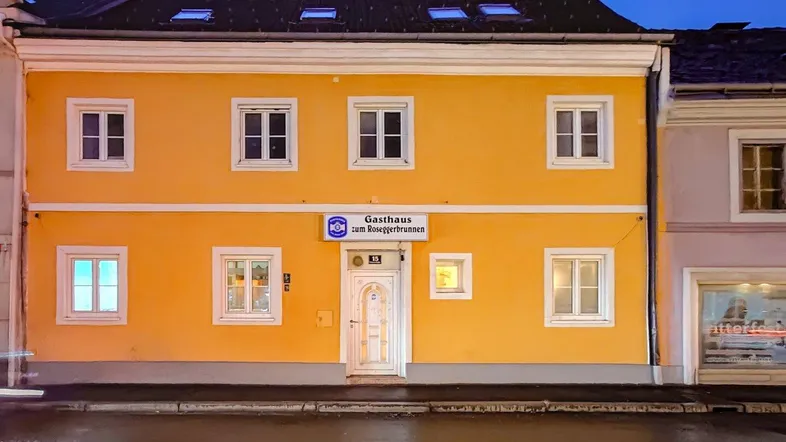 Gelbe Fassade eines traditionellen Gebäudes mit vielen Fenstern und einem Gasthaus-Schild am Abend.