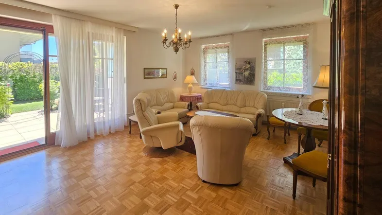 Gemütliches Wohnzimmer mit Parkettboden, beigen Sofas und Zugang zur Terrasse und zum Garten.