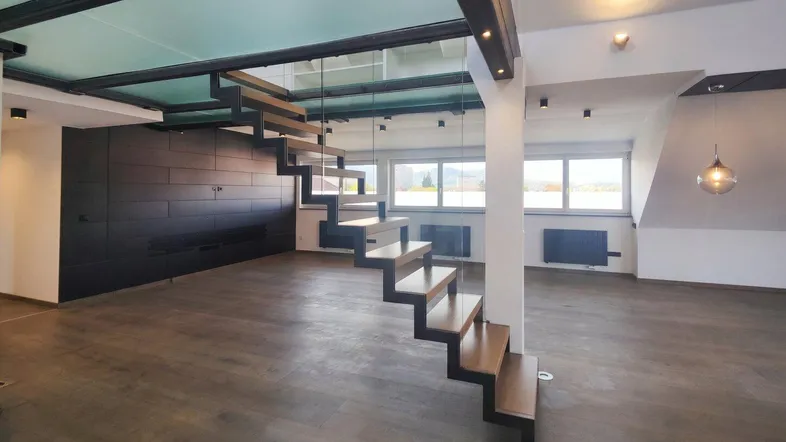 Geräumiges Wohnzimmer mit moderner Treppe, Holzboden und großen Fenstern mit Ausblick.