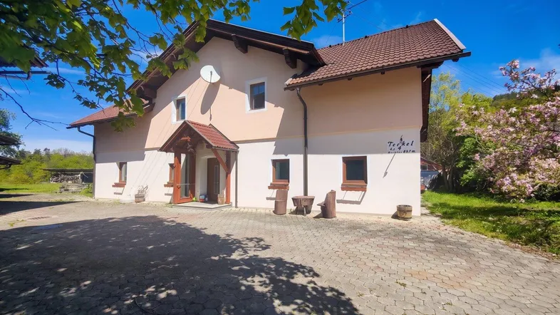 Traditionelles Haus mit gepflastertem Vorplatz und grüner Umgebung unter blauem Himmel.
