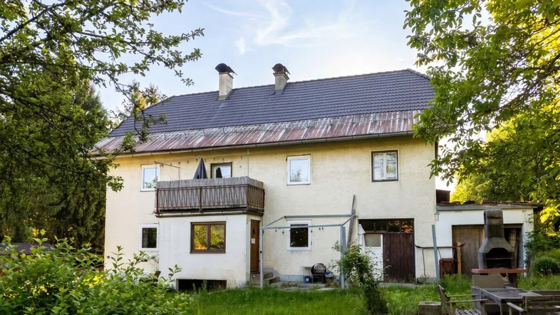 Hinteransicht des Hauses mit Garten, Grillplatz und Balkon unter blauem Himmel.