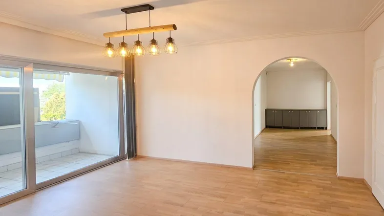 Helles Wohnzimmer mit Parkettboden, Zugang zum Balkon und einem modernen Deckenleuchter.