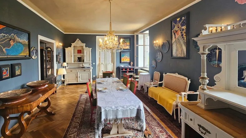Elegantes Esszimmer mit großem Esstisch, Kronleuchter und Fischgrätparkett, umgeben von Kunstwerken.