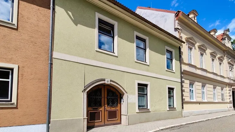 Grünes Gebäude mit traditioneller Fassade und Holztüren an einer ruhigen Straße.