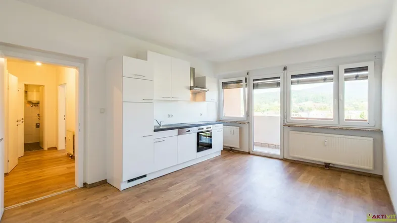 Heller Wohnraum mit integrierter Küchenzeile, Laminatboden und Zugang zum Balkon.