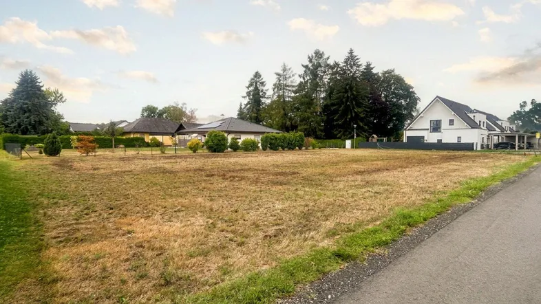 Weitläufiges Grundstück mit trockenem Gras und umliegenden Wohnhäusern unter bewölktem Himmel.