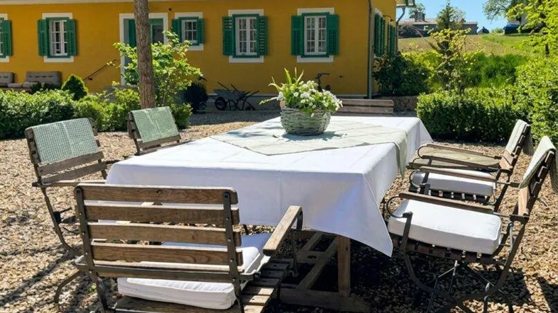 Gemütlicher Essbereich im Freien auf Kiesboden mit Blick auf das charmante gelbe Haus.