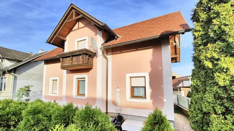 Seitenansicht des Hauses mit gepflegten Büschen und einem kleinen Balkon im Obergeschoss.