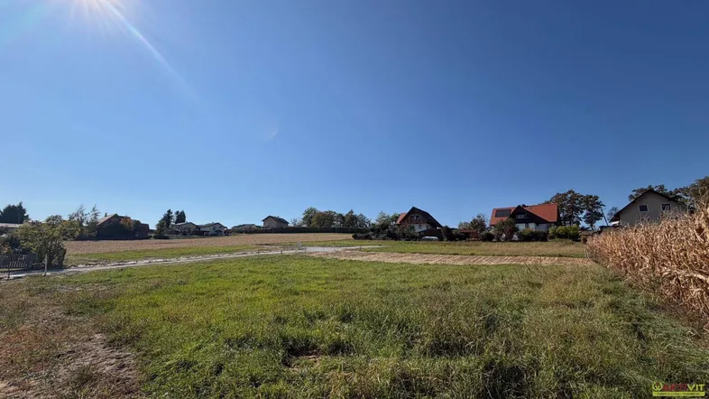 Weitläufiges Grundstück mit grüner Wiese und Häusern im Hintergrund unter strahlend blauem Himmel.