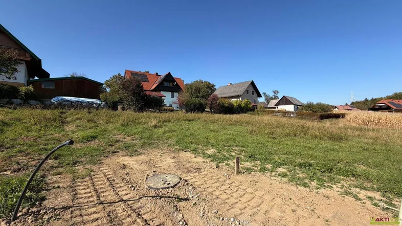 Grundstück mit vorbereitetem Baugrund, umgeben von ländlicher Bebauung unter blauem Himmel.