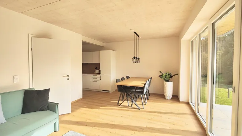 Heller offener Wohn- und Essbereich mit Holzboden, moderner Einrichtung und Zugang zur Terrasse.