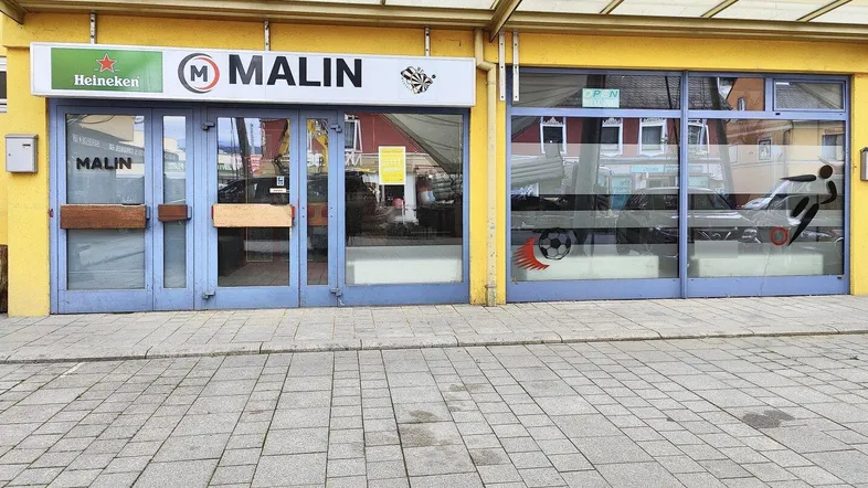 Außenansicht eines Geschäftsgebäudes mit großen Schaufenstern und Werbeschildern an der Fassade.