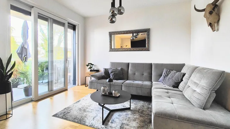 Helles Wohnzimmer mit modernem Sofa, Holzboden und Zugang zum Balkon.