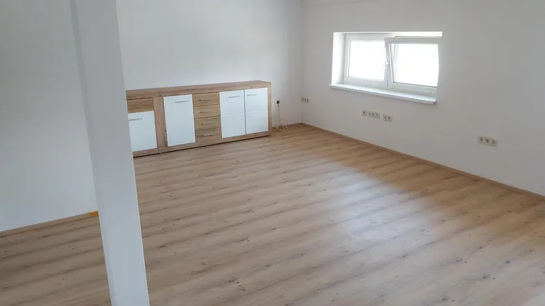 Heller, leerer Raum mit Laminatboden, weißen Wänden und einem Fenster, bereit zur Einrichtung.
