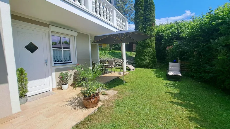 Gepflegter Gartenbereich mit Terrasse, Liegestühlen und Sonnenschirm, ideal zum Entspannen im Freien.