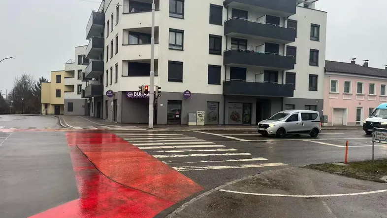 Modernes Mehrfamilienhaus mit Balkonen und Geschäften im Erdgeschoss an einer belebten Straßenkreuzung.