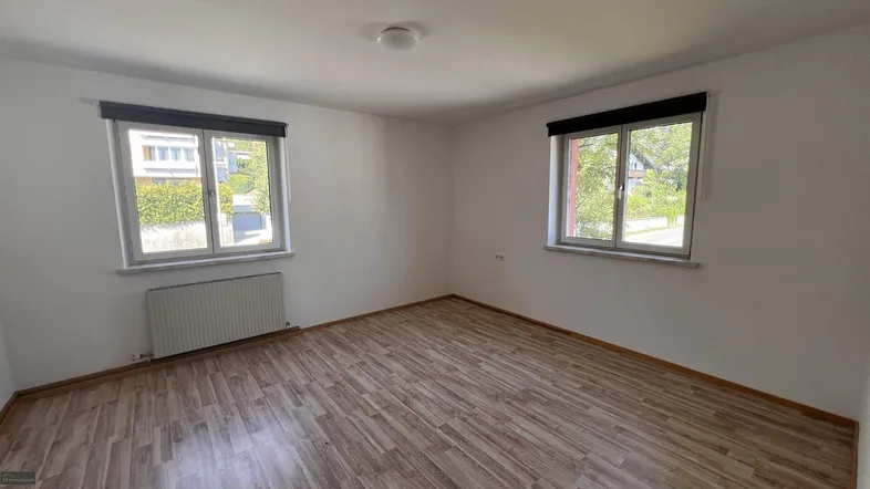 Helles Zimmer mit Laminatboden und zwei Fenstern, die viel Tageslicht hereinlassen.