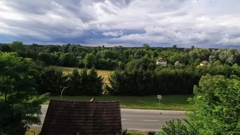 Weitläufiger Blick über grüne Landschaft und Dächer unter einem bewölkten Himmel.