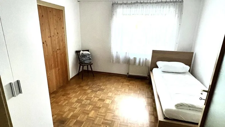 Helles Schlafzimmer mit Parkettboden, Einzelbett und weißem Kleiderschrank, ideal für Gäste oder Kinder.