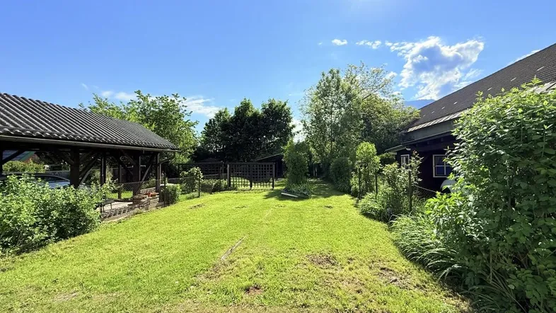 Grüner Gartenbereich mit Rasenfläche und einem überdachten Sitzplatz unter blauem Himmel.