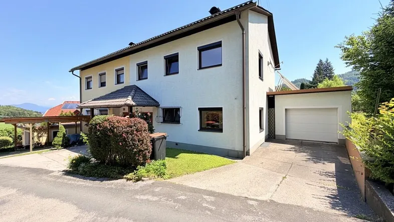 Einfamilienhaus mit weißer Fassade, Garage und Carport in ländlicher Umgebung.