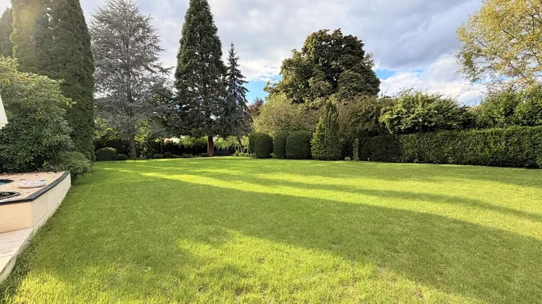 Großer, gepflegter Rasenbereich mit hohen Bäumen und Hecken, der zum Entspannen einlädt.