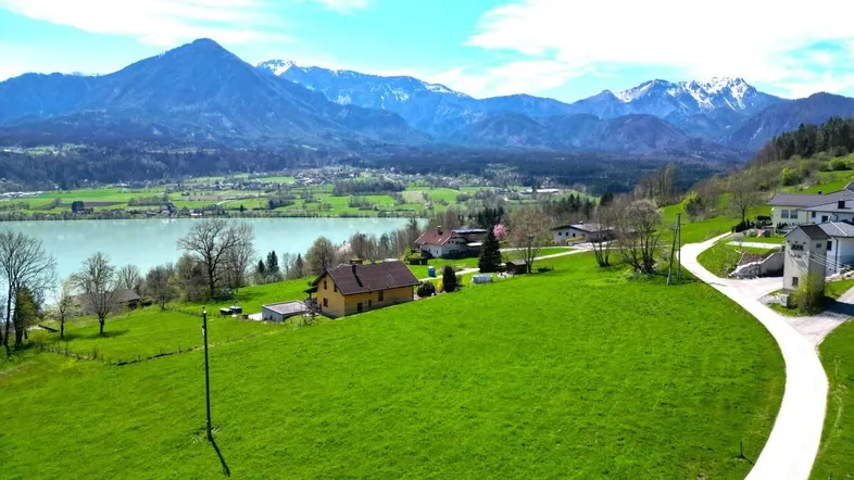 Panoramablick auf ein Grundstück mit weiten Grünflächen, See und majestätischer Bergkulisse.