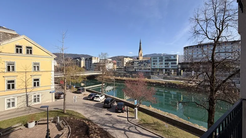 Panoramablick über den Fluss und die Stadt mit historischen Gebäuden und Bergen im Hintergrund, genossen von einem Balkon.