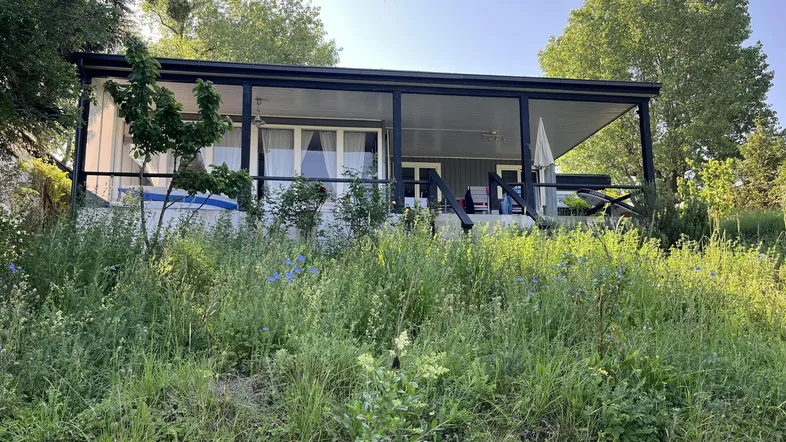 Charmantes Haus mit überdachter Terrasse und üppiger Vegetation in sonniger Lage.