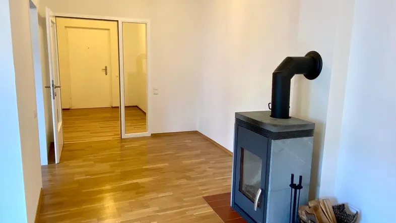 Helles Wohnzimmer mit modernem Kaminofen und Parkettboden, der zu weiteren Räumen führt.