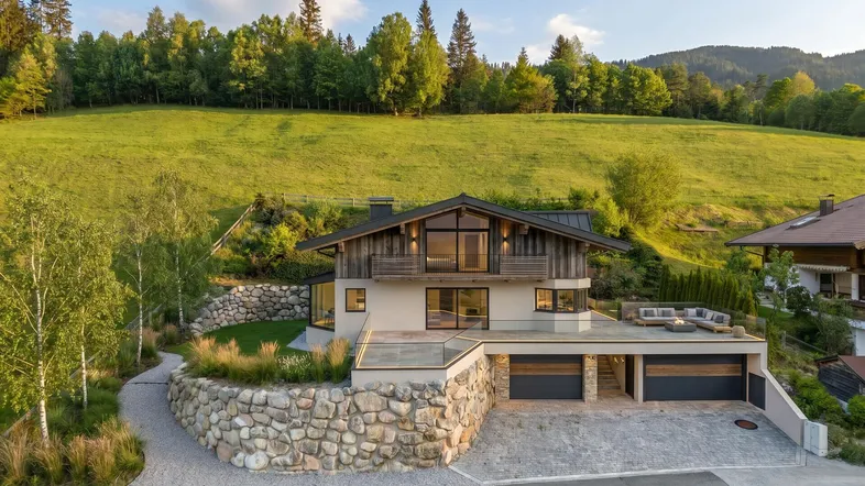 Modernes Chalet mit großer Terrasse, Steinfassade und weitem Blick auf die umliegende Natur.
