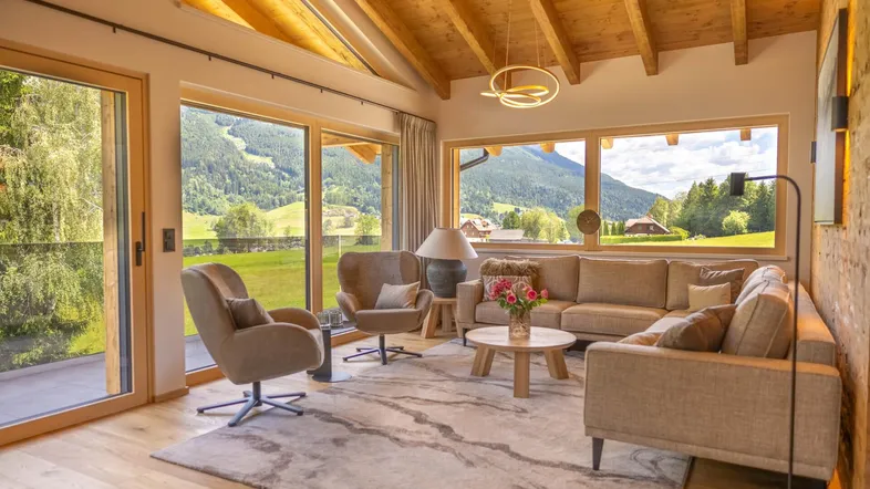 Helles Wohnzimmer mit Holzbalkendecke, großen Fenstern und Bergblick in modernem Design.