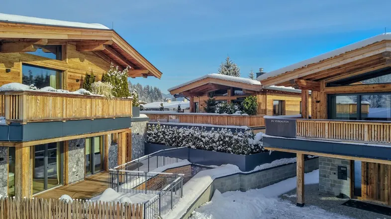 Moderne Chalets mit Holzfassaden und schneebedeckten Dächern in alpiner Umgebung.