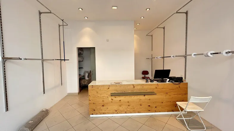 Heller Ladenraum mit Holztresen, weißen Wänden und flexiblen Kleiderstangen, ideal für ein Geschäft.