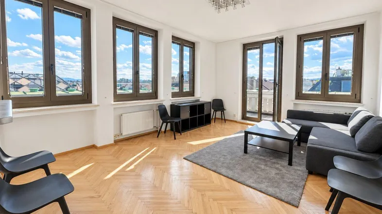 Helles Wohnzimmer mit Fischgrätparkett, großen Fenstern und Zugang zu einem französischen Balkon.