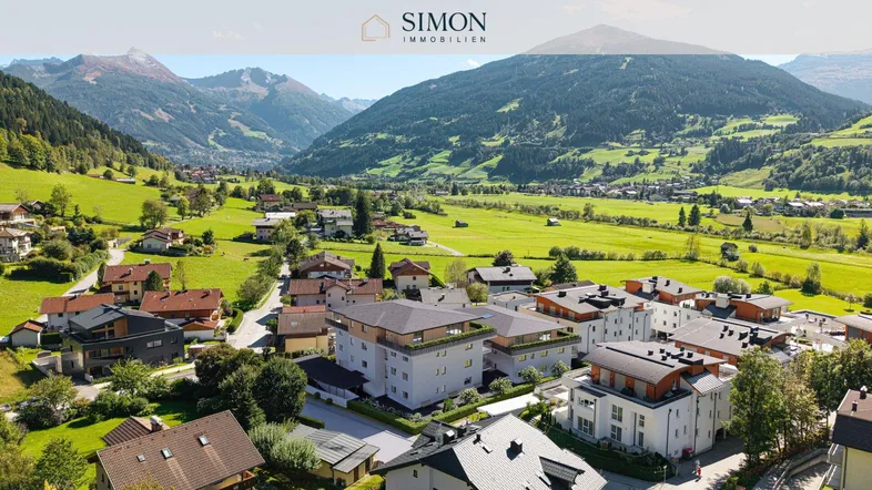 Luftaufnahme eines charmanten Dorfes in einem grünen Tal, umgeben von majestätischen Bergen.