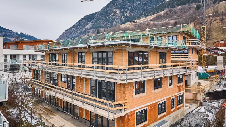 Mehrfamilienhaus im Bauzustand mit Gerüst und Blick auf die umliegenden Berge.