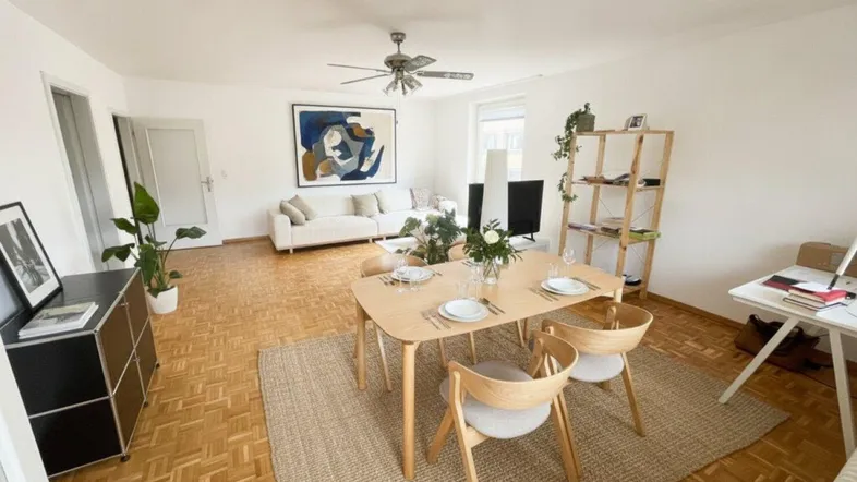 Helles Wohn- und Esszimmer mit Parkettboden, moderner Einrichtung und Deckenventilator.