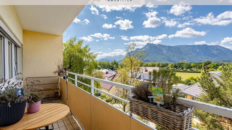 Heller Balkon mit Holztisch und Stühlen, bietet einen weiten Blick auf die umliegende Berglandschaft.
