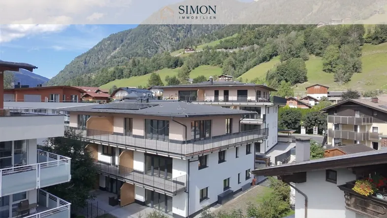 Modernes Apartmentgebäude mit Balkonen und Blick auf die umliegende Berglandschaft.