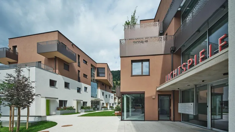 Moderne Wohngebäude mit braun-weißen Fassaden und einem gepflasterten Innenhof, inklusive Kinoeingang.