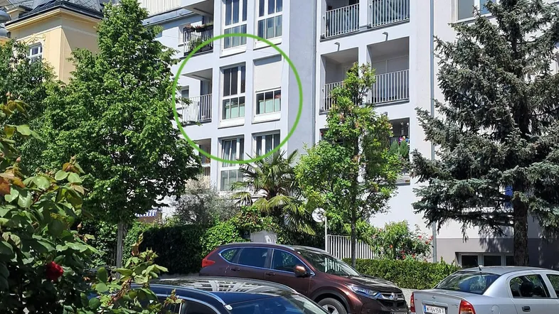 Modernes Wohngebäude mit Balkonen und großen Fenstern, umgeben von Grünflächen und parkenden Autos.