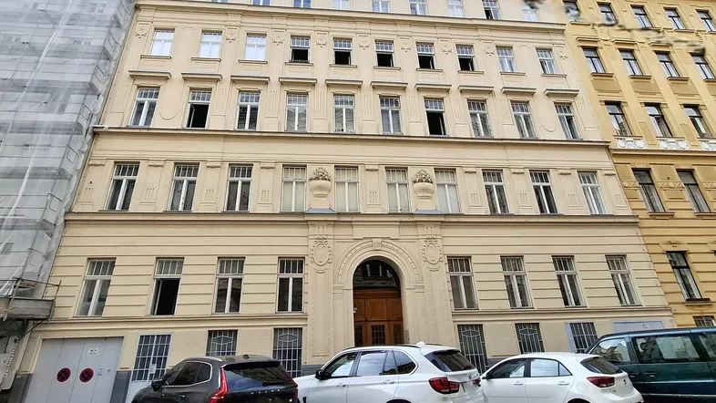 Historische Fassade eines Mehrfamilienhauses mit klassischer Architektur und parkenden Autos davor.