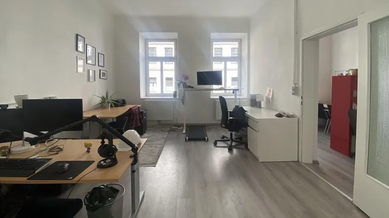 Geräumiges Büro mit mehreren Arbeitsplätzen, hellen Wänden und großen Fenstern, die viel Tageslicht hereinlassen.