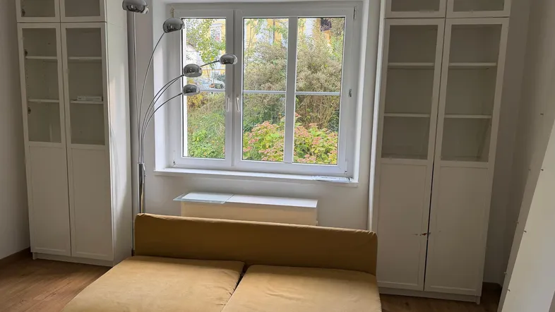 Helles Wohnzimmer mit Sofa, Bücherregalen und Blick ins Grüne durch das große Fenster.