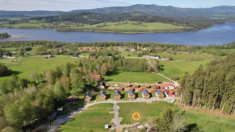 Luftaufnahme einer Siedlung von Häusern am Seeufer mit umliegenden Wäldern und Bergen im Hintergrund.